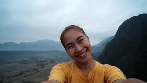 Cheerful enthusiastic Asian tourist girl turn around in Pha Ngeun, Vang Vieng, Laos. Young woman have fun and happy sightseeing on the top of mountain with beautiful landscape and nature. Selfie shot.