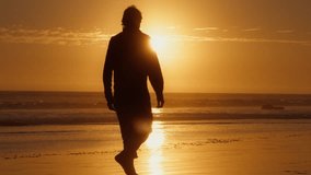 Silhouette of man walking barefoot on beach at sunset. Back view of guy enjoying sea landscape in golden hour. Male tourist looking sunrise on sandy shore. Ocean waves rolling on coast in slow motion  - Powered by Shutterstock - Get 15% off with code: PIKWIZARD15