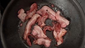 Bacon strips frying in a pan, changing color.