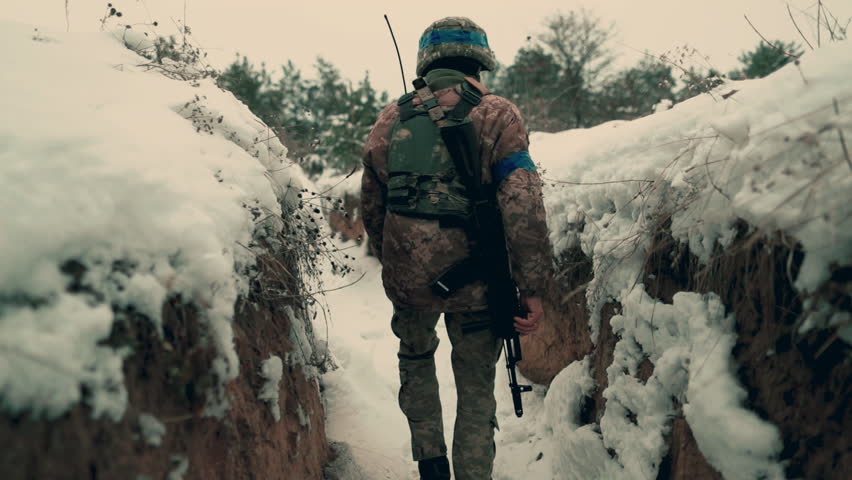 A soldier with a machine gun walks along the trench. A soldier in full armor walks along a trench. A soldier in the field. soldier with weapon in war.