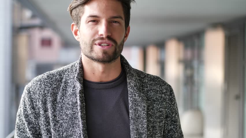 One handsome young man in urban setting in European city, standing, smiling and talking to the camera
