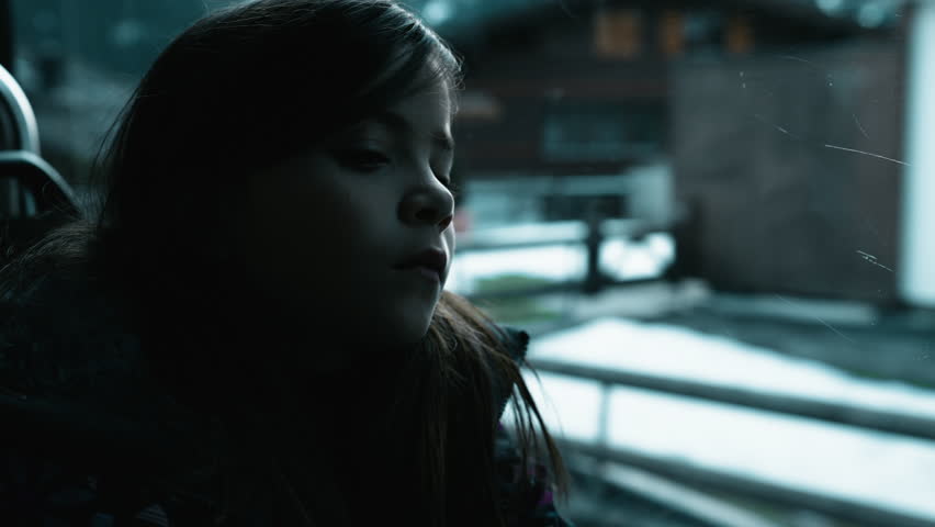 Depressed child travels by bus struggling in sadness by window. Passenger little girl in thoughtful melancholic emotion inside moving transportation