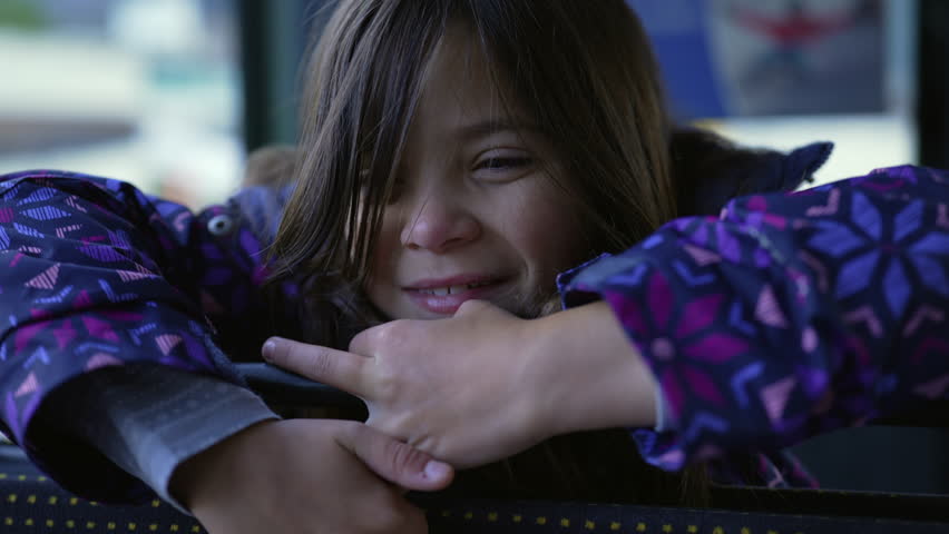 Closeup of a pensive happy little girl face leaning on bus seat smiling. Thoughtful 8 year old child