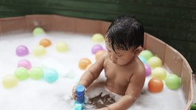 Baby having fun taking bath playing in water with foam with colorful toys.