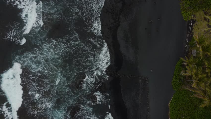 Overhead shot of waves crashing on black sand beach