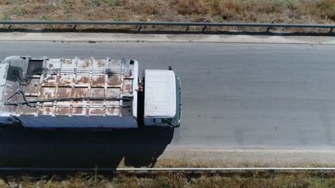 Aerial top-down view flight over road then garbage truck takes over other common names for this type of truck include trash truck rubbish truck waste collection vehicle and refuse collection vehicle