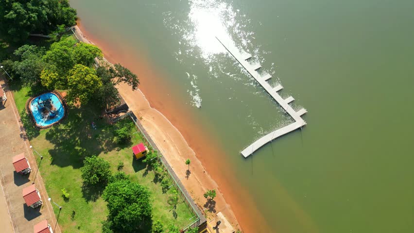 Aerial view of the river beach in Porto de Maringa, on the Parana River. We can watch the sun reflecting on the river with people bathing,Brasil - tilt, drone shot