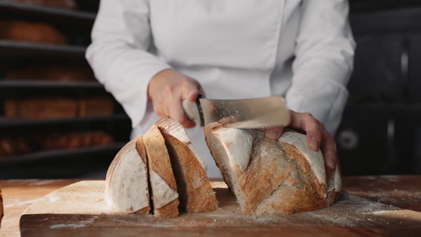 Woman chef cutting healthy bread on wooden board at bakehouse kitchen