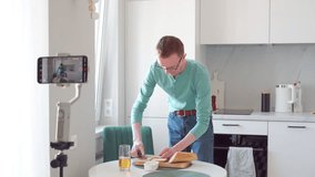 Lonely man in morning, in kitchen, he shoots breakfast on phone camera. He's making toast, there's glass of juice next to it. Modern technologies. Professions online. 4k footage.