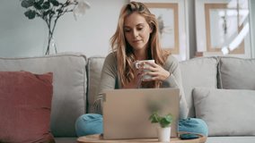 Video of beautiful young woman working with her laptop while drinking a cup of coffee sitting on a couch at home - Powered by Shutterstock - Get 15% off with code: PIKWIZARD15