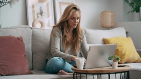 Video of beautiful young woman working with her laptop while drinking a cup of coffee sitting on a couch at home - Powered by Shutterstock - Get 15% off with code: PIKWIZARD15
