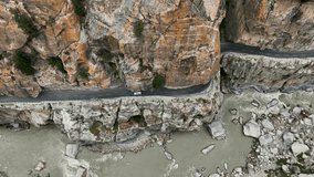 Aerial video by a drone over a dangerous road along a river between the gorges in a steep valley in rocky mountains. High quality 4K video.