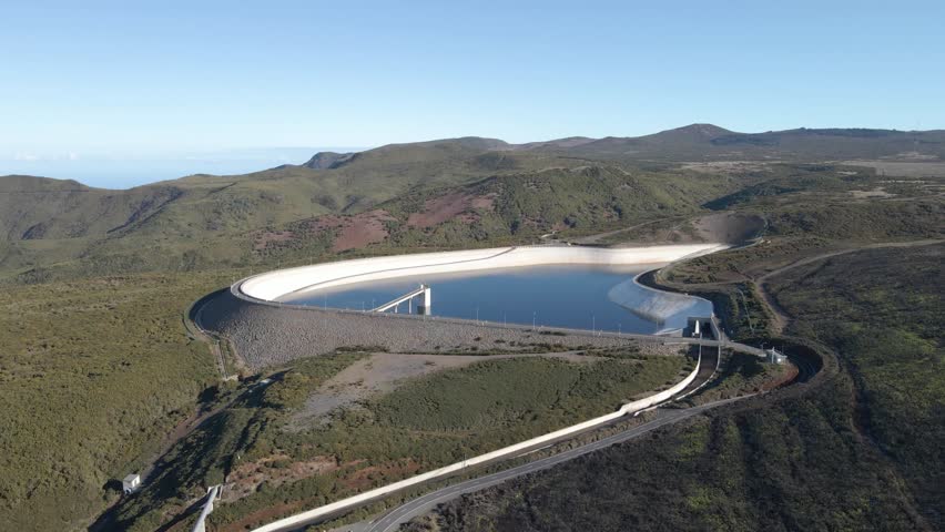 Aerial view of the Paul da Serra water reservoir built to harvest the rainwater. Drone rotating to the left showing the green mountains and the blue sky in the background. 
