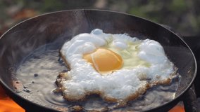 Fresh egg is fried in a frying pan outdoors with a sizzling oil and smoke on an open fire, close up - Powered by Shutterstock - Get 15% off with code: PIKWIZARD15