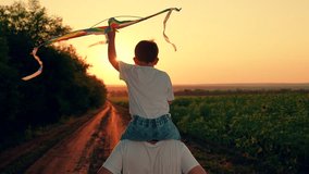 Son plays dreams of fly, traveling, Happy boy on dad shoulders runs along country road, plays with toy kite, sunset. Child, dad is running with kite, sun. Kite floats in child hand. Kid with toy kite - Powered by Shutterstock - Get 15% off with code: PIKWIZARD15