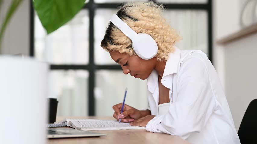 E-learning,online education concept.Happy student in headphones writing down lectures,doing homeworl,listening to podcast etc