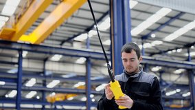 Young man using control in a factory. Worker manipulating crane in workplace