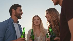 Joyful friends clinking beers relaxing together on rooftop party close up. Diverse group people laughing talking at weekend gathering. Happy team holding alcohol drinks relaxing at evening hang out. - Powered by Shutterstock - Get 15% off with code: PIKWIZARD15