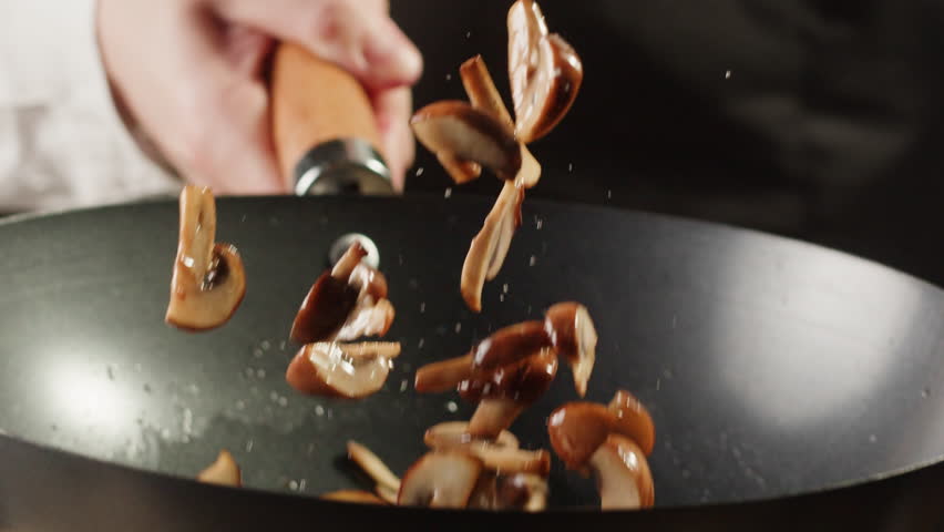 Chef cooking mushrooms on wok frying pan close up. Champignons mushroom with salt in pan. Restaurant Food concept