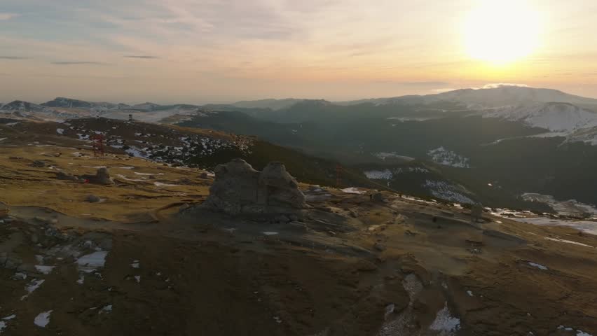 aerial orbit cinematic shot of romnian bucegi sphinx with tourists  next to it in carpathian mountains during sunset