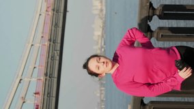 Young chubby female drinks water after intense running and nordic walking training in city park. Hydration concept. Vertical video. Charming woman in sportswear drinking water from bottle
