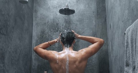 Man washing in shower back view. Man washes head and body in shower, gray bathroom. Morning procedures before work, study, hygiene, washing foaming cleaning of hair, head, scalp. Back view, rear view.: film stockowy