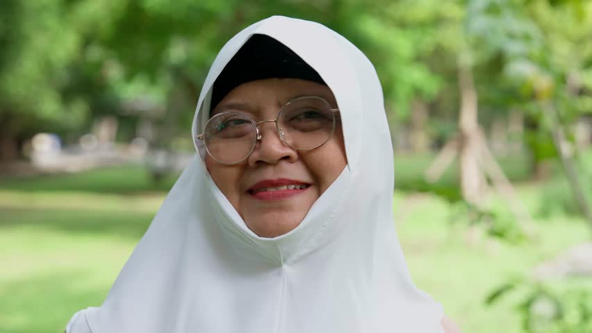 Closeup face of cheerful elderly woman covered with headscarf smiling outdoors. Casual Islamic girl in park. Freedom and relaxing outdoors. Happiness, smile, and face of Islamic female person with joy Royalty-Free Stock Footage #3409378615