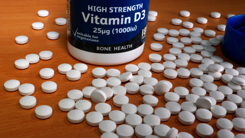 Closeup dolly shot of a white tablets or pills spread out next to an unbranded high strength Vitamin D tub or container.