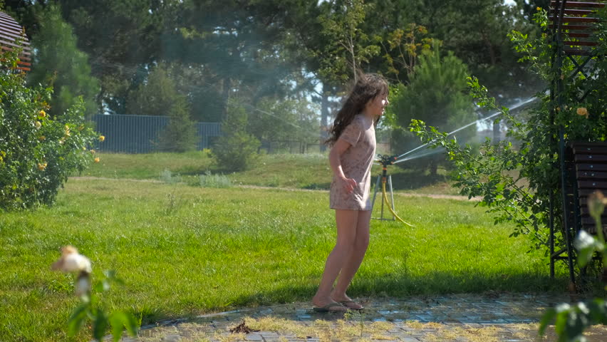 Resting in water sprinkles in the park. A view of smiling child with fun resting in the water sprinkle in the green park lawn in the sun light.