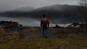 motivational video man walking backwards opens his arms with the sea in the background between mountains with fog