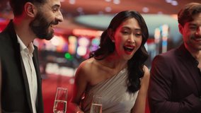 Handsome Hispanic Man Clinking Champagne Glasses With Beautiful Asian Woman In Fancy Dress Standing Next To Roulette Table In Luxurious Casino. Couple Celebrating Winning Bet Among Other Gamblers. - Powered by Shutterstock - Get 15% off with code: PIKWIZARD15