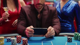 Handsome Man in Suit Uses Smartphone for Online Casino Blackjack Betting, Celebrates Victory with Two Elegant Women. Lucky and Happy Young People Cheering in a Luxurious Casino. Glamorous People