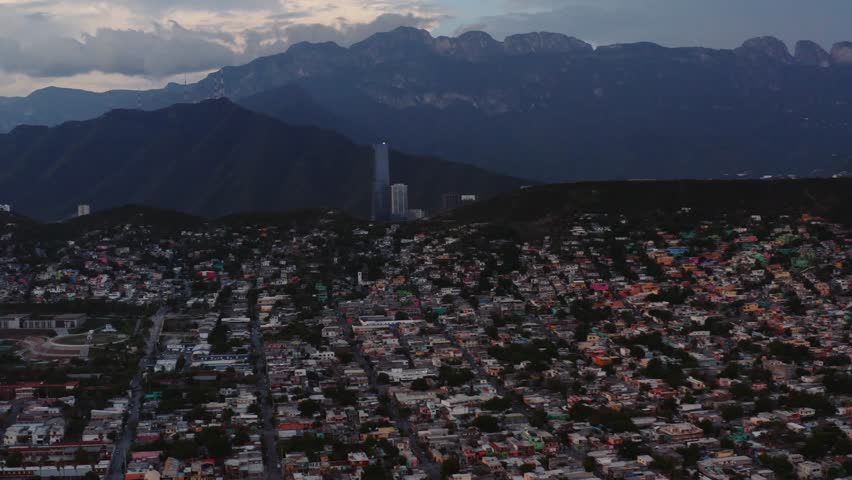 Wide aerial view of sprawling Monterrey, Mexico. Urban city center with backdrop of steep mountains and sunset sky. Stunning landscape surrounding second largest city in Mexico.