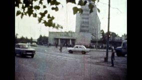 Public transport, cars drive along road in summer street background. Car traffic against of city landscape backdrop. Early morning auto rush in highway. Vintage color film. Urban archive. Retro 1980s