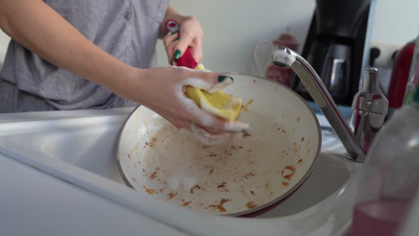 Hands young woman washing dirty greasy frying pan in sink, in home kitchen