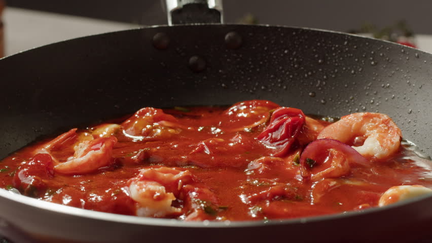 Tomatoes with red hot peppers, lime juice and shrimps are languishing in a pan. Traditional Asian Mexican Thai dish. High quality studio shot macro close-up. Cooking Italian pasta.