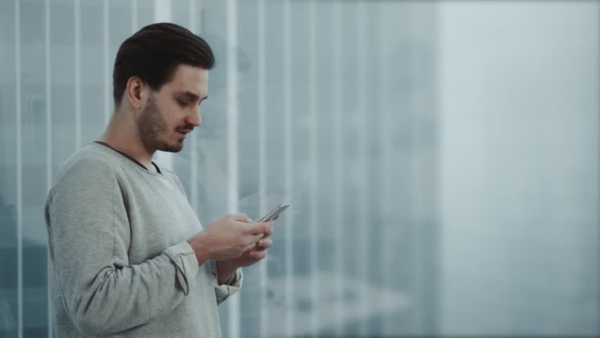 Portrait of young businessman talk on cellphone while stand by his office window in modern interior of skyscraper building, male entrepreneur having mobile phone conversation after important briefing Royalty-Free Stock Footage #34096858