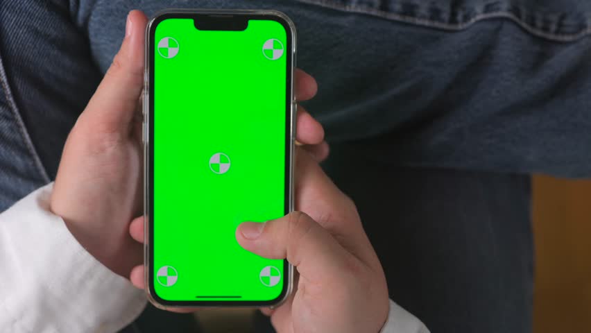 Close-up of a hand holding a smartphone with a green screen, ideal for app mockups.