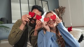 Smiling young couple covering their eyes with red heart shaped papers, having fun at Valentine Day. Boyfriend and girlfriend celebrating their love relationship together on a romantic date at home - Powered by Shutterstock - Get 15% off with code: PIKWIZARD15