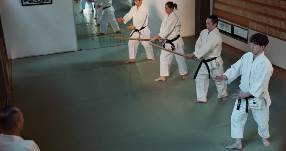 People, sensei and practice with weapon in dojo for fighting, training or karate class. Martial arts group with trainer or master in stancing for etiquette, attitude or commitment with black belt