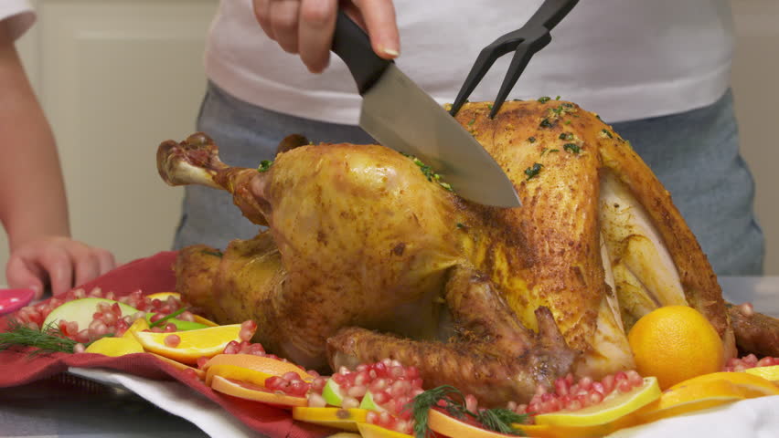 woman carving roasted stuffed turkey and slicing cuts of turkey, preparing thanksgiving or christmas holiday dinner