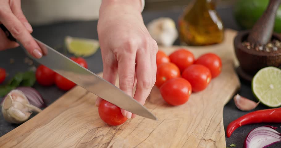 Salsa recipe - Woman cutting cherry tomatoes for salad on wooden board with kitchen knife