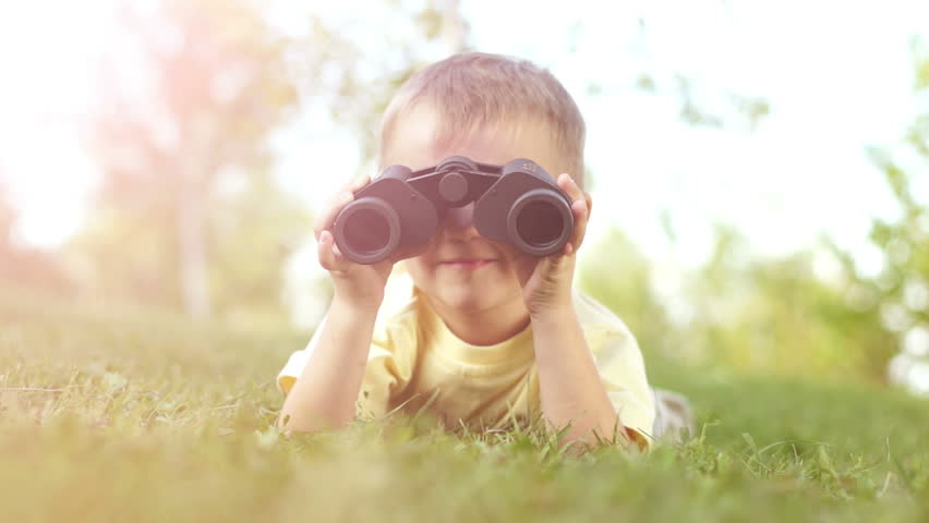 Closeup portrait of a little boy looking through binoculars outdoors. Sunny