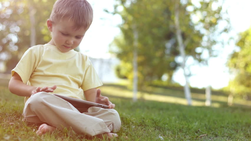 Cute boy using a touchpad pc outdoors. Child sittning on the grass in sun