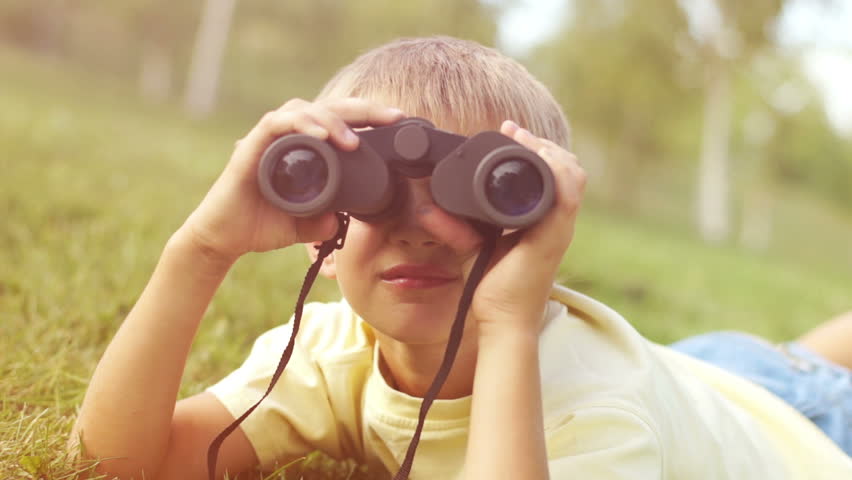 Closeup portrait of a boy looking through binoculars at camera in sunny lights
