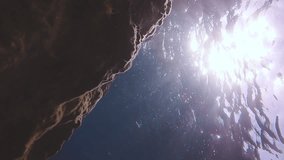 Vertical video, Marine waves crashing on coastal rock reef on bright sunrays. Seascape with sunbeams penetrating through sea waves near coastal cliff, Underwater shot - Powered by Shutterstock - Get 15% off with code: PIKWIZARD15