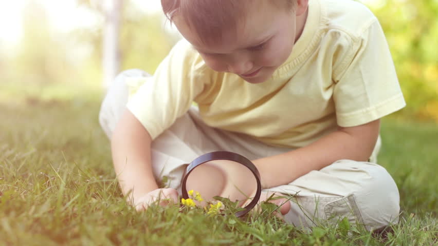 Close-up portrait of a little boy with a magnifier. Sitting on the grass in sun
