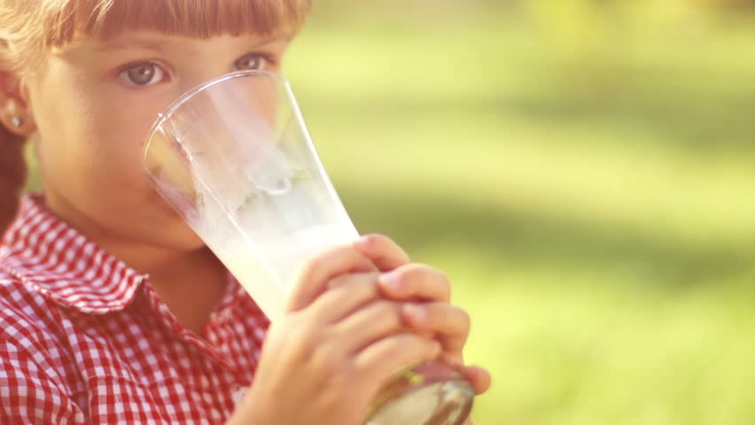Portrait of smiling girl drinking milk outdoors in sunny lights. Milk mustache.
