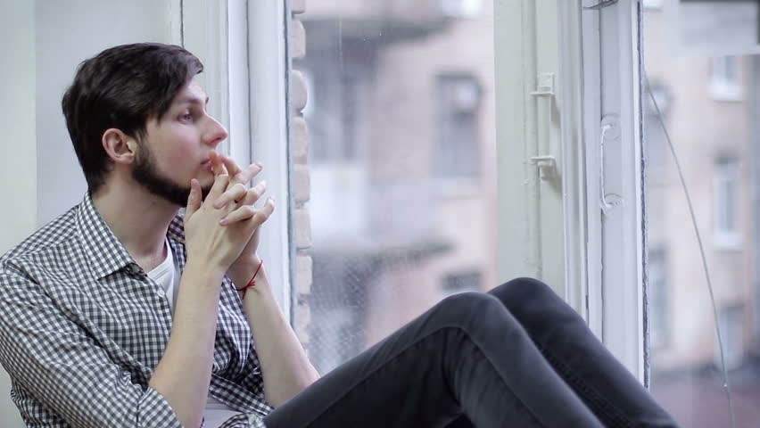 Sad guy sitting on the windowsill and looking out the window | Shutterstock HD Video #34101208