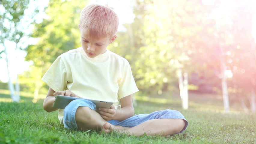 Boy online using a tablet computer outdoors in sunny lights
